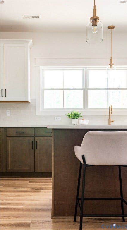 Kitchen island featuring a light-toned countertop, a gold-toned faucet, and clear glass pendant lighting