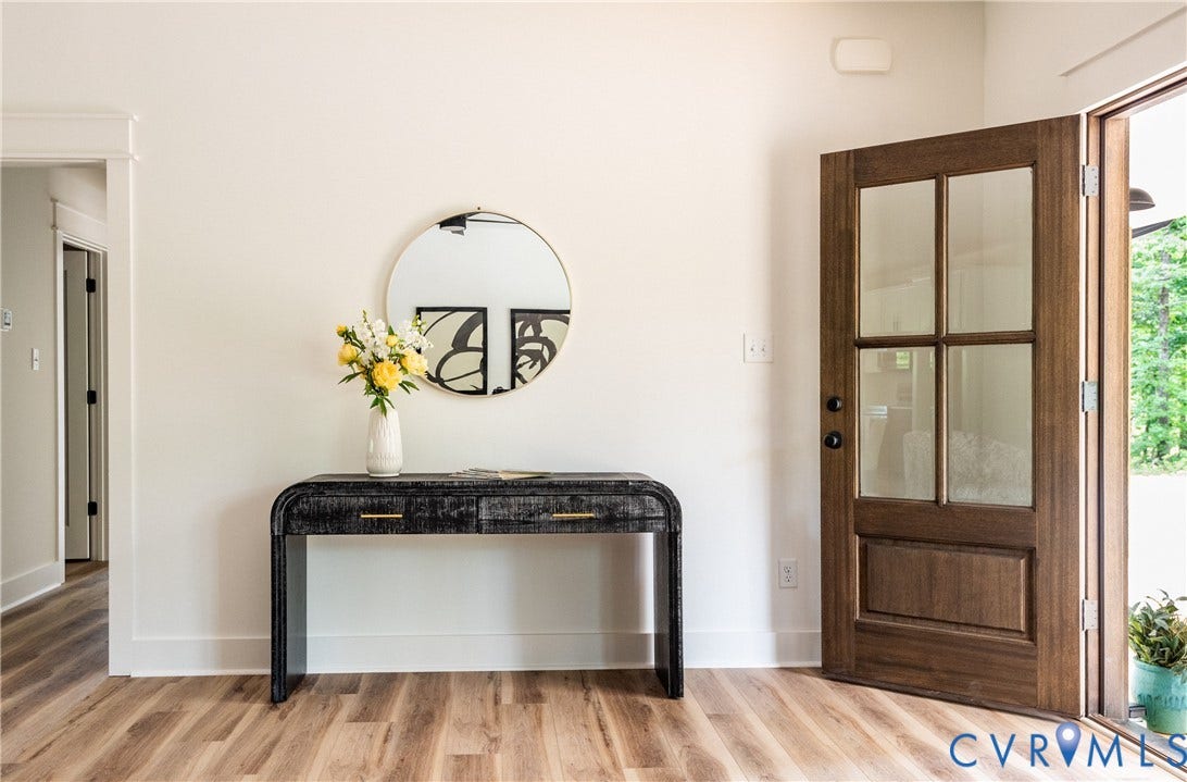 Warm LVP flooring complements the solid wood entry door with glass panels