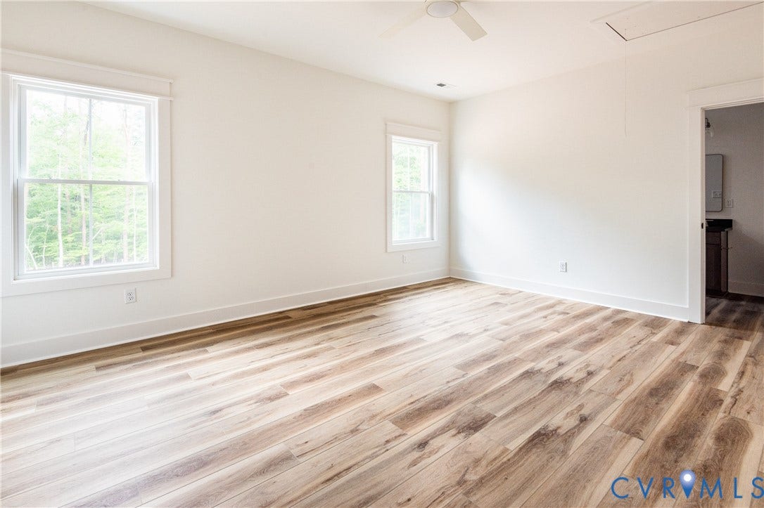 Bright room featuring LVP flooring, two large windows, a ceiling fan, and white baseboards