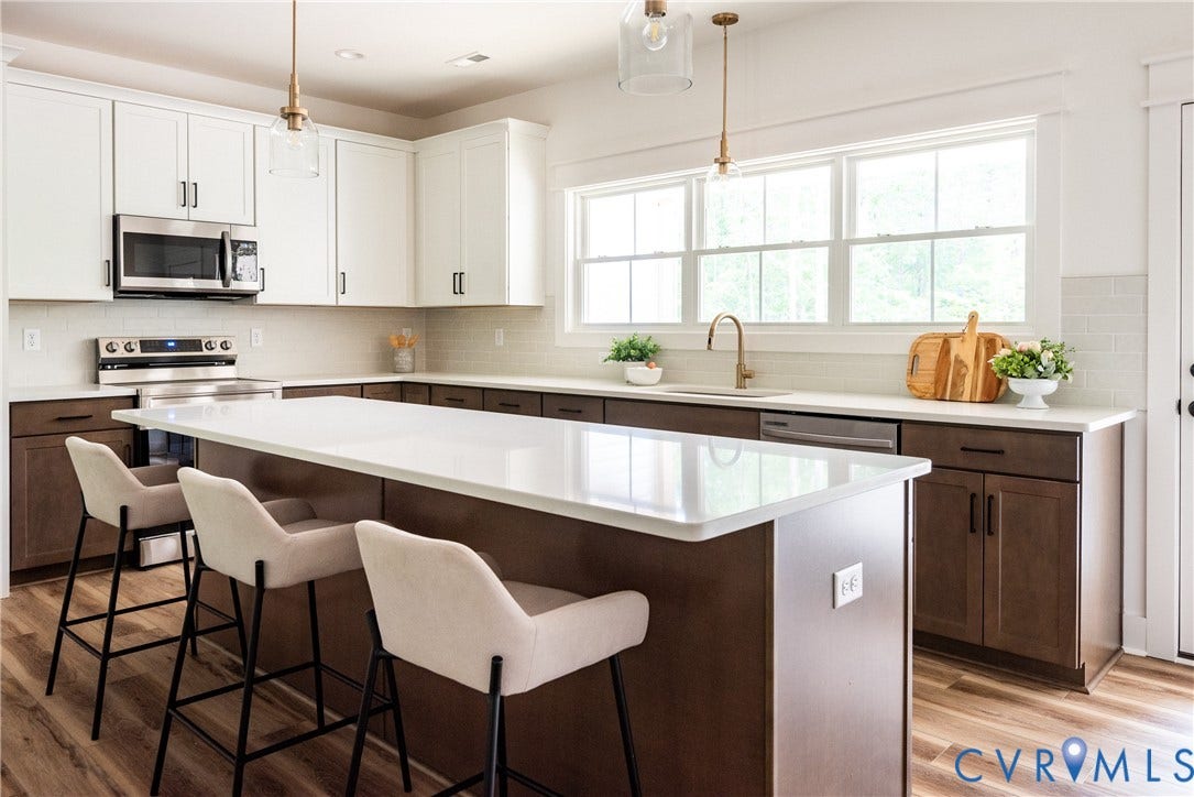 Spacious kitchen featuring a large central island with seating, stainless steel appliances, a white subway tile backsplash, and ample natural light from multiple windows