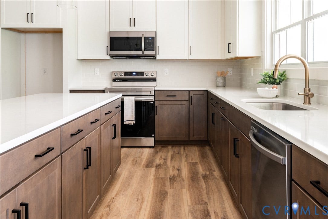 Modern kitchen featuring a large island, stainless steel appliances, white countertops, two-tone cabinetry, and LVP flooring