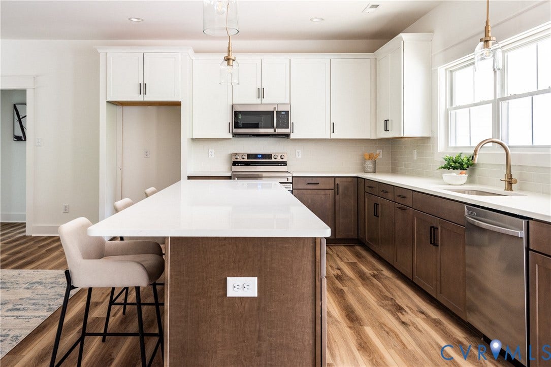 Contemporary kitchen featuring a large central island with seating, two-tone cabinetry, stainless steel appliances, and LVP flooring