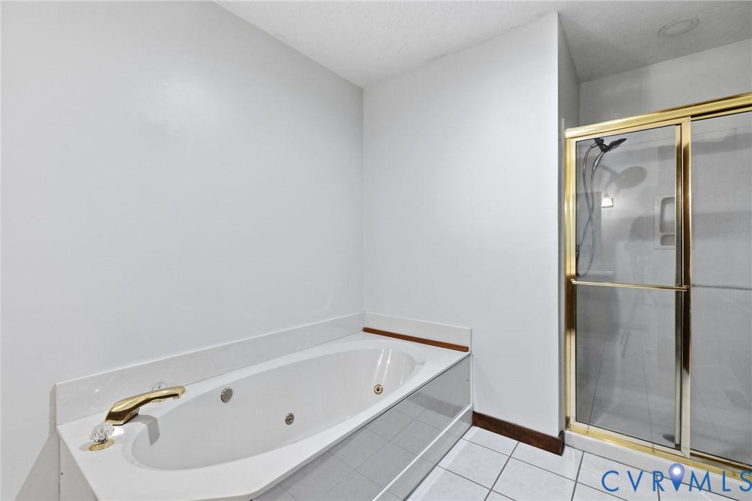 White built-in jetted tub with gold-tone fixtures and a surrounding white countertop, complemented by a separate glass-enclosed shower with gold-tone framing
