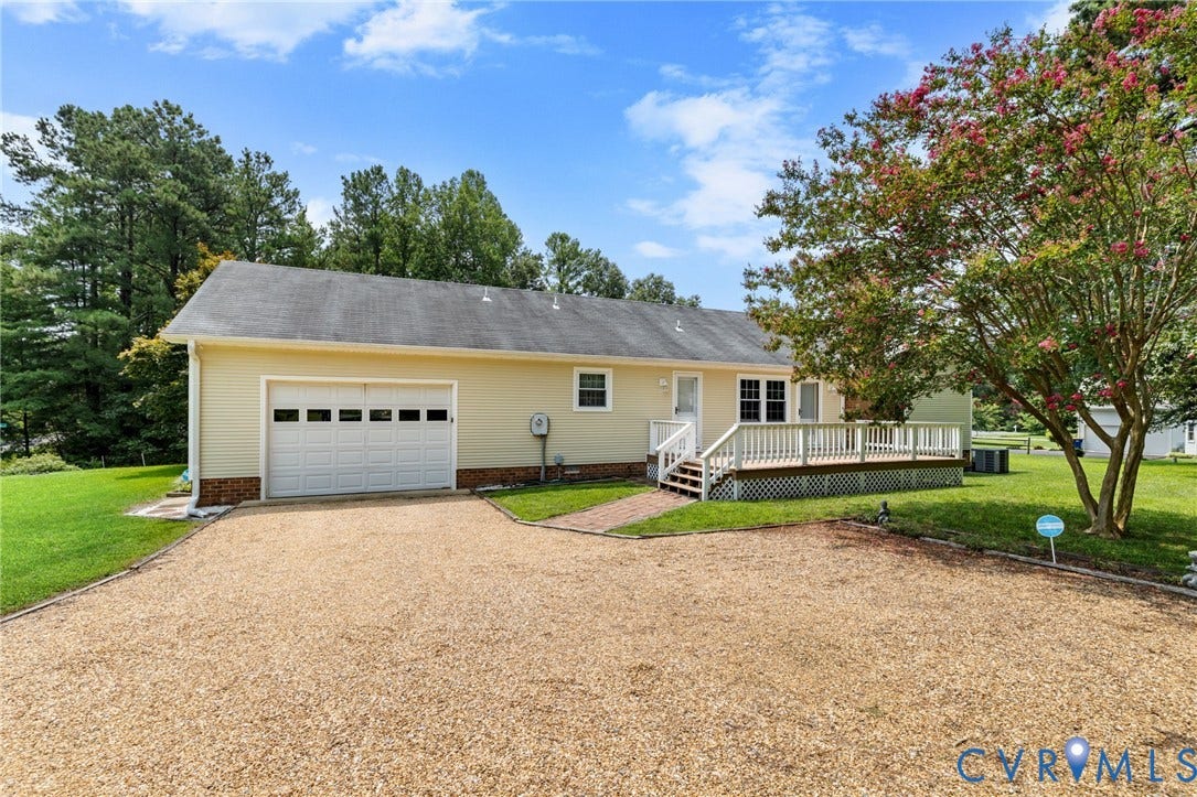 Ranch-style exterior with a gravel driveway, attached garage, and a large wooden deck