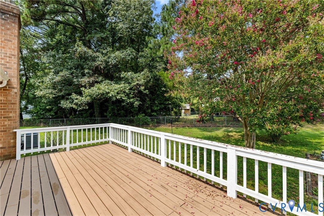 Expansive wood-finish deck with white railing, overlooking a lush green yard and mature trees, including a blooming crepe myrtle