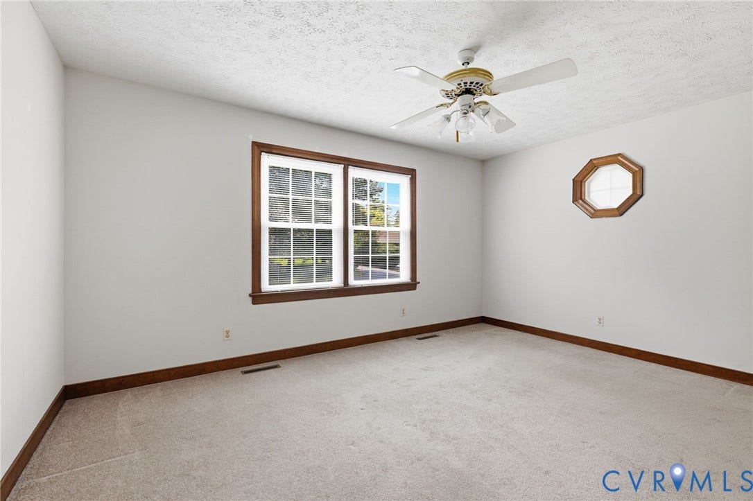 Spacious room featuring neutral carpeting, white walls, and a large double window with wood trim