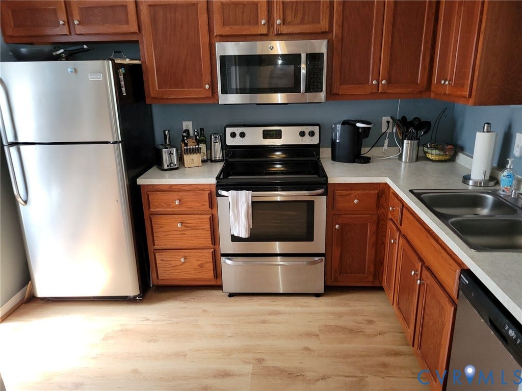 4900 Finnegan Court, Henrico, VA 23228 Kitchen featuring wood-finish cabinetry, light-toned countertops, and stainless-steel appliances including a refrigerator, range, microwave, and double basin sink