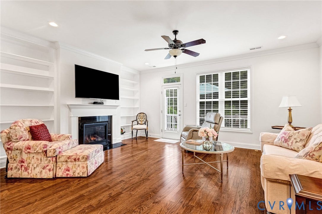 14379 Michaux Village Drive, Winterfield Park, Midlothian, VA 23113 Spacious living area featuring rich wood-finish flooring, a central fireplace with a mantel, built-in shelving, a ceiling fan, and abundant natural light from multiple windows