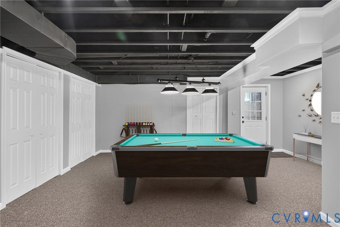 381 Shorewood Drive, Shorewood, Mineral, VA 23117 Finished lower level featuring a dark-stained pool table, dark exposed ceiling joists, neutral carpet, white paneled doors, and a glass-paned door. Virtually staged.