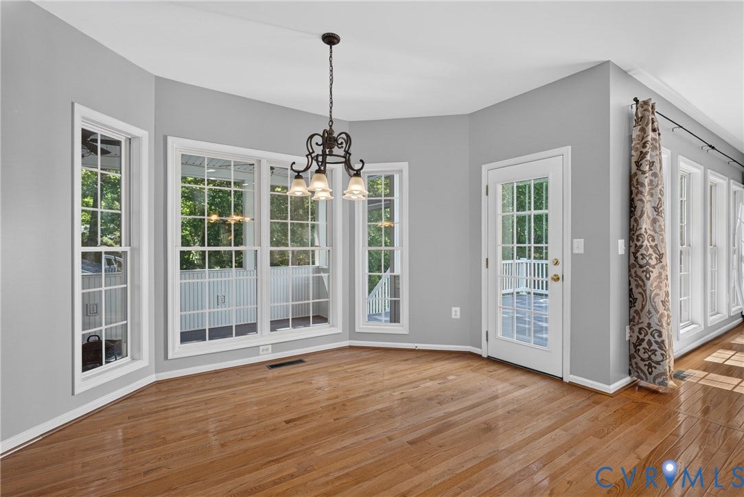 381 Shorewood Drive, Shorewood, Mineral, VA 23117 Spacious room featuring hardwood flooring, multiple windows providing abundant natural light, a glass-paned door opening to an outdoor deck, a prominent chandelier, and light gray wall paint