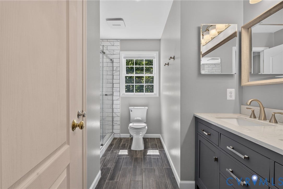 381 Shorewood Drive, Shorewood, Mineral, VA 23117 Hall bathroom featuring wood-finish flooring, a vanity with a light countertop and brushed nickel fixtures, a glass-enclosed shower with subway tile, a window, and a wall-mounted mirror