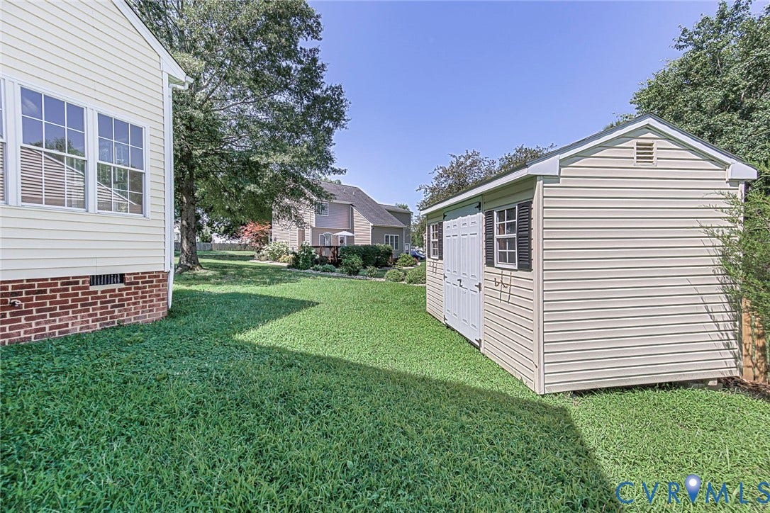 Detached storage shed featuring vinyl siding, gable roof, and double doors with decorative shutters