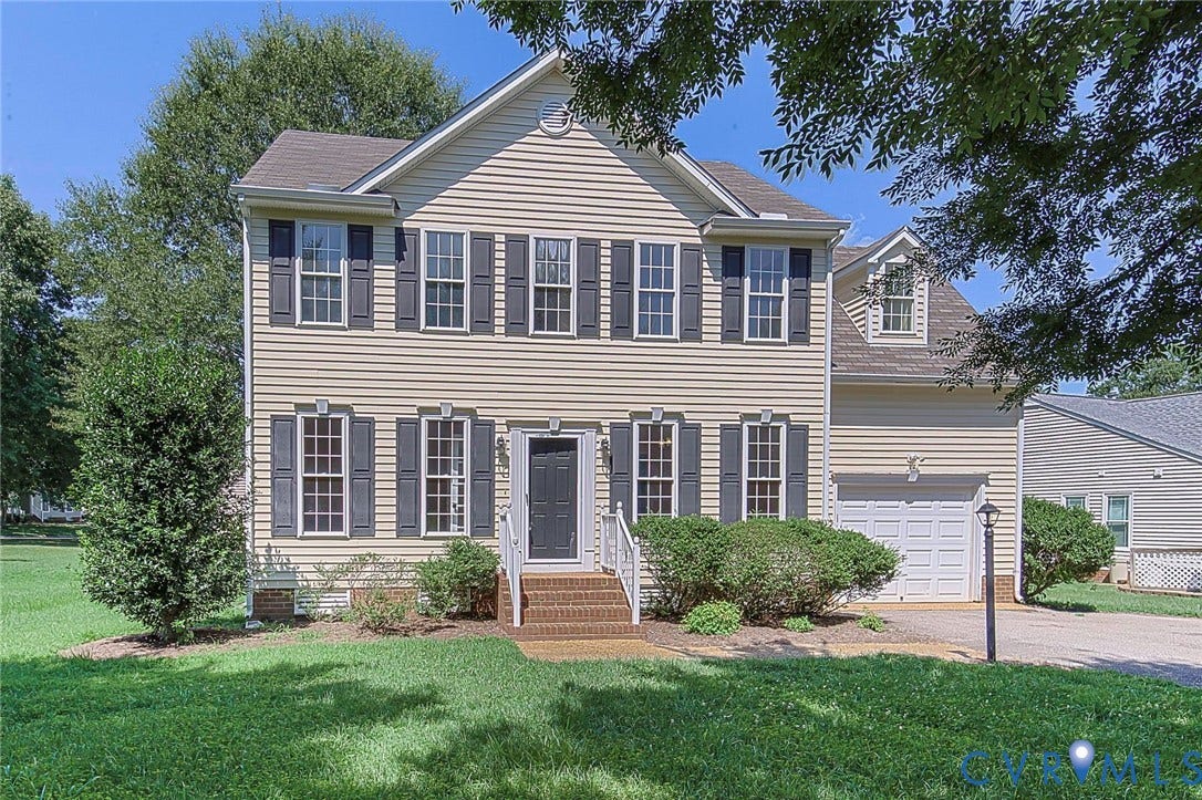 Traditional two-story residence featuring light-colored siding, black louvered shutters, an attached garage, and a dormer window