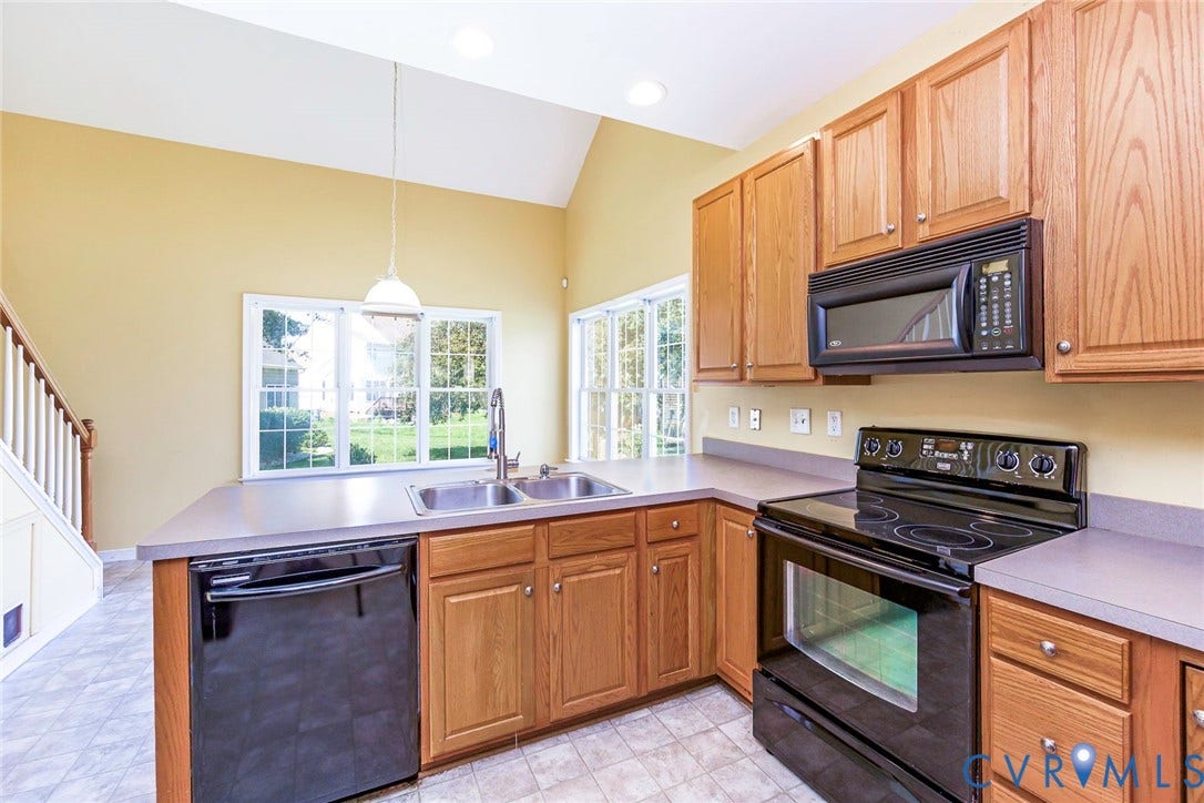 Kitchen featuring wood cabinetry, a double basin sink, black appliances, and a vaulted ceiling