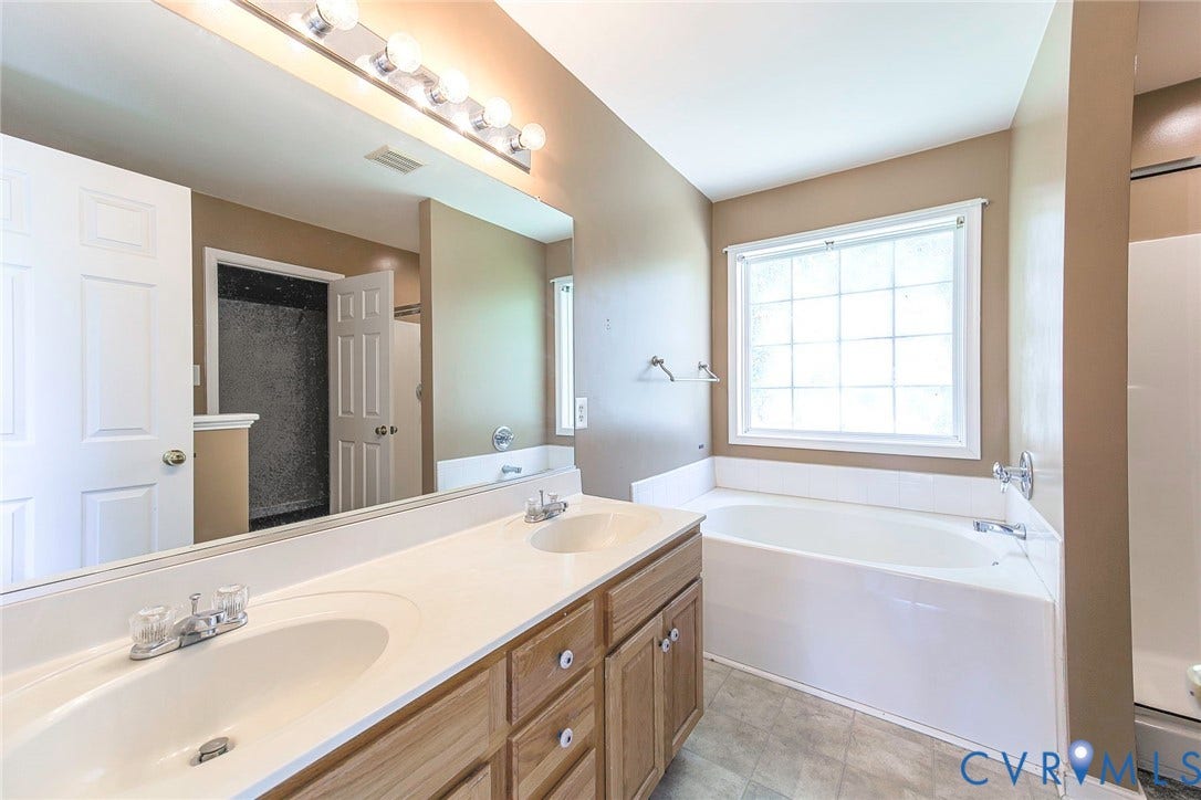 Bathroom featuring a dual vanity with a light wood-finish cabinet and integrated sinks, a built-in bathtub, a privacy window, and a separate shower enclosure
