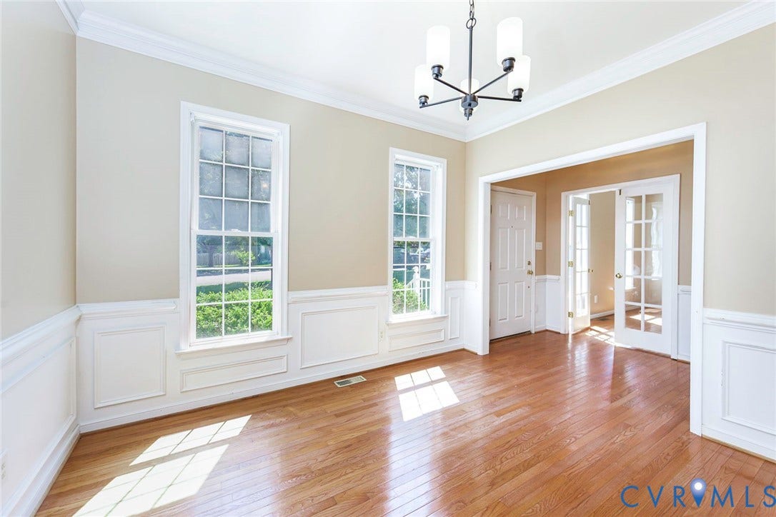 Spacious room featuring wood-finish flooring, two large windows, white wainscoting, and crown molding