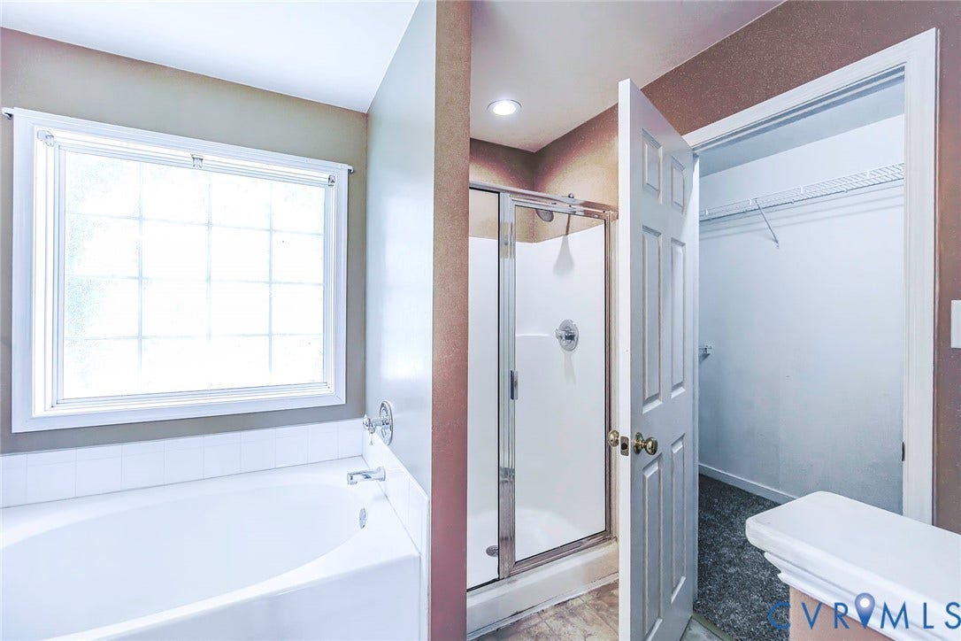 White soaking tub with chrome fixtures, a frosted window, and an adjacent enclosed shower with a glass door