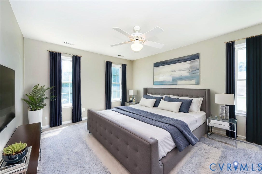 Spacious room with a ceiling fan, three windows with dark draperies, and light-colored walls