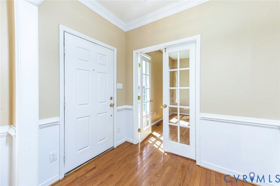 Entryway featuring wood-finish flooring, wainscoting, crown molding, a paneled entry door with brass hardware, and double French doors opening to an interior room