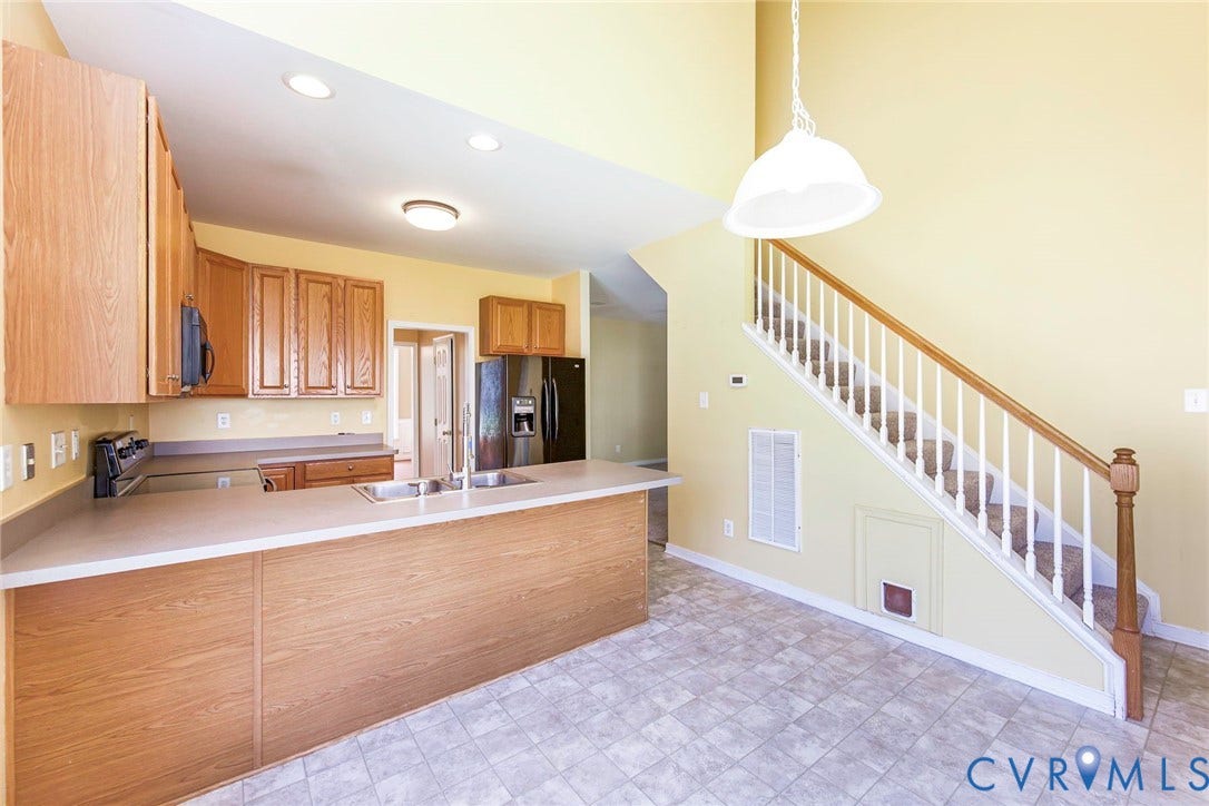 Open-concept kitchen and living area featuring a breakfast bar with dual sinks, wood-finish cabinetry, black appliances, and recessed lighting