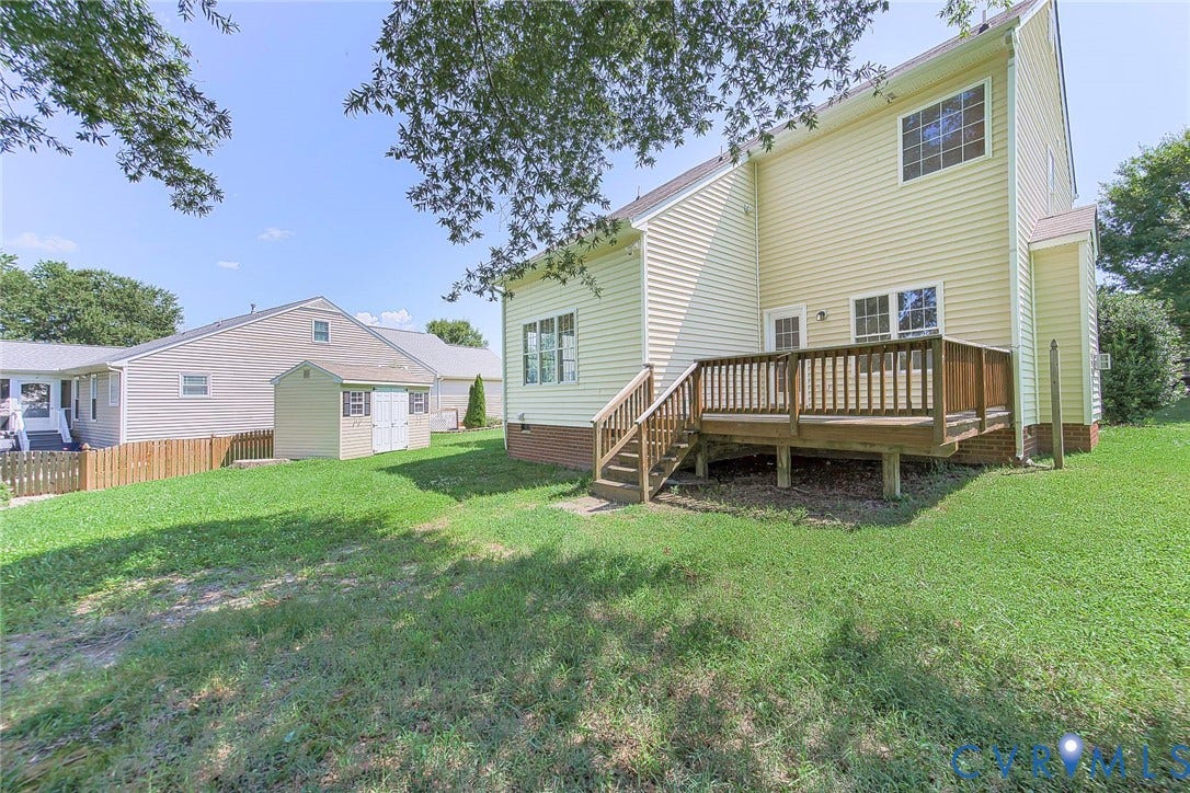 Rear exterior featuring a wooden deck with railing, siding, multiple windows, and a detached storage shed