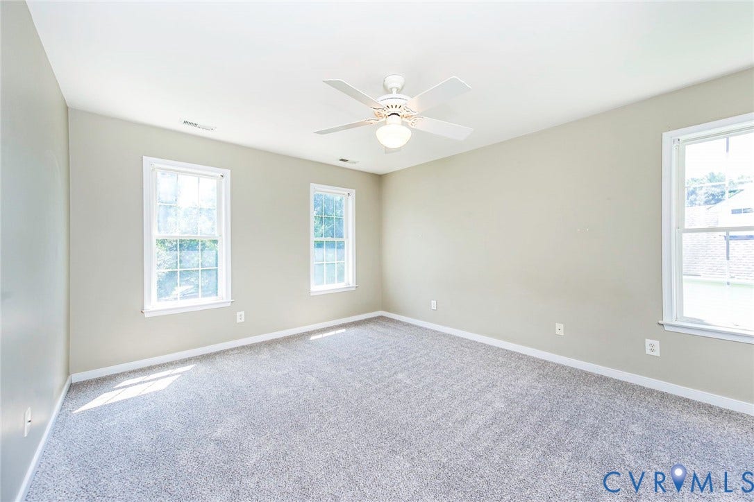 Spacious room featuring light gray wall paint, gray carpeting, and white baseboards