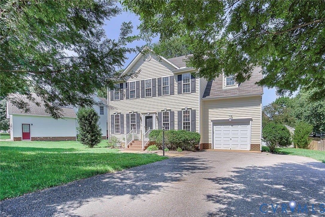 Traditional two-story residence featuring light-colored siding, dark window shutters, a front entry porch with white railings, a paved driveway, and an attached single-car garage