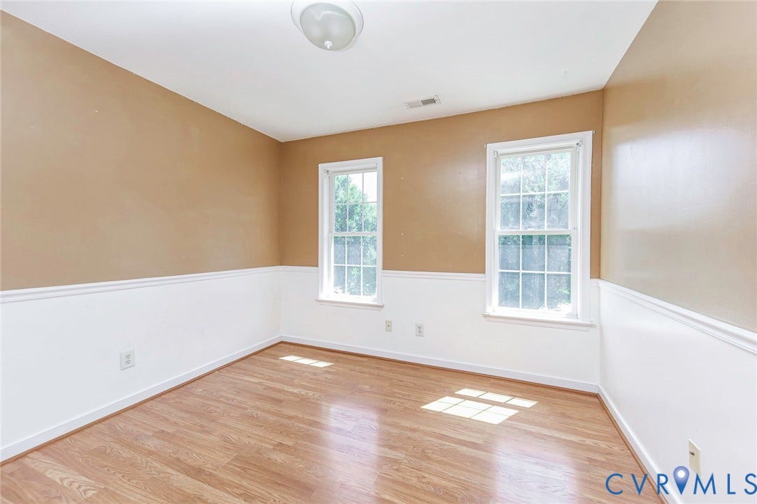 Interior room featuring two double-hung windows, wood-finish flooring, and two-tone walls with wainscoting