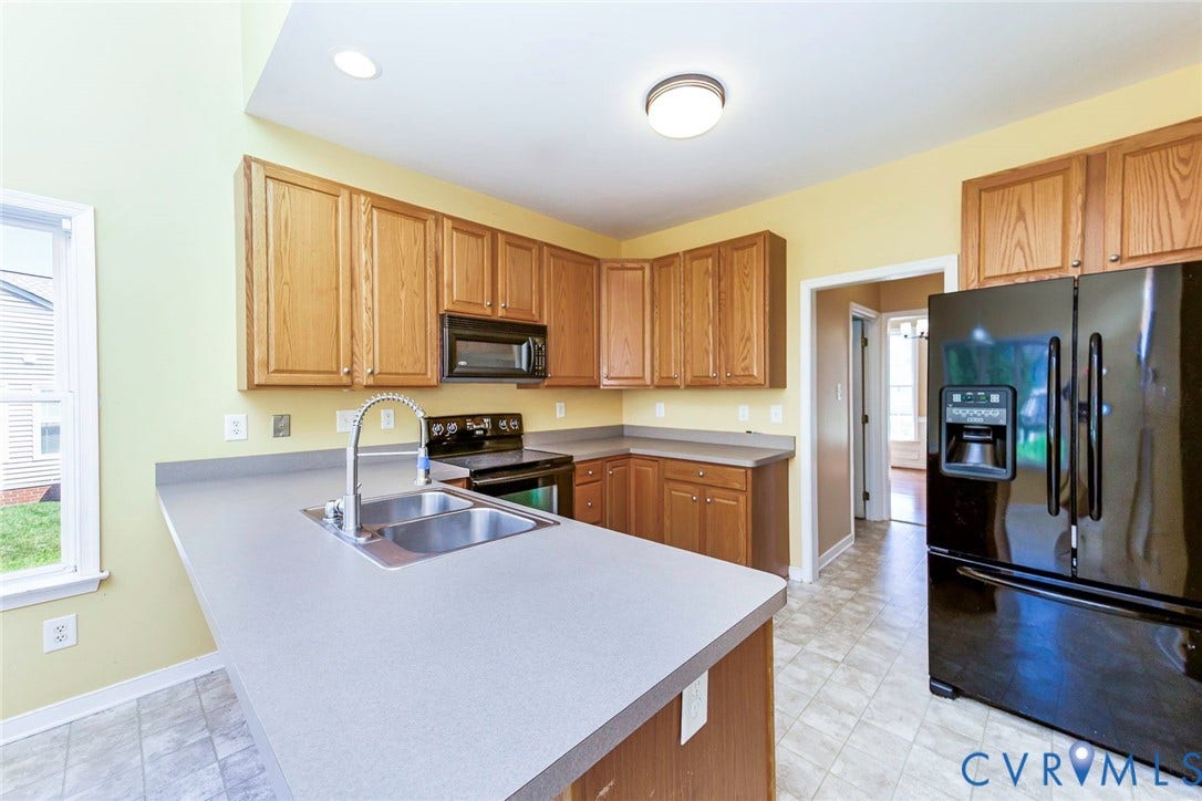 Kitchen featuring wood-finish cabinetry, a black appliance suite, laminate countertops, and a double-basin stainless steel sink with a gooseneck faucet