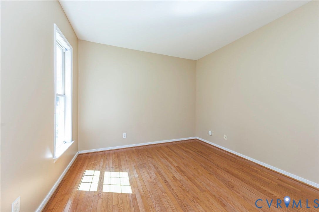 Room featuring wood-finish flooring, a double-hung window with white trim, and light beige wall paint