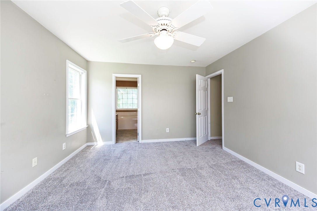 Spacious room featuring light gray wall paint, light-colored carpet flooring, and white trim