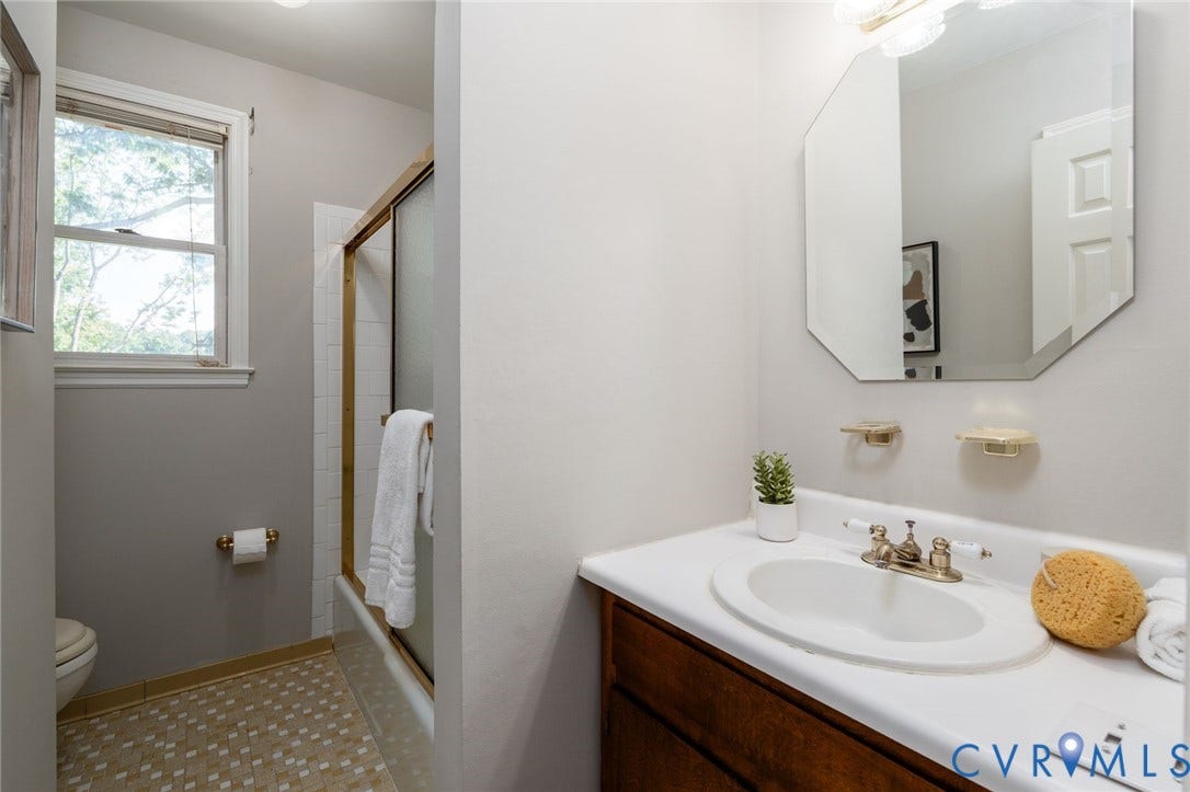 14613 Gimbel Drive, Chester, VA 23836 Bathroom featuring a vanity with an integrated white sink, an octagonal wall mirror, a window, and a shower with a sliding glass door