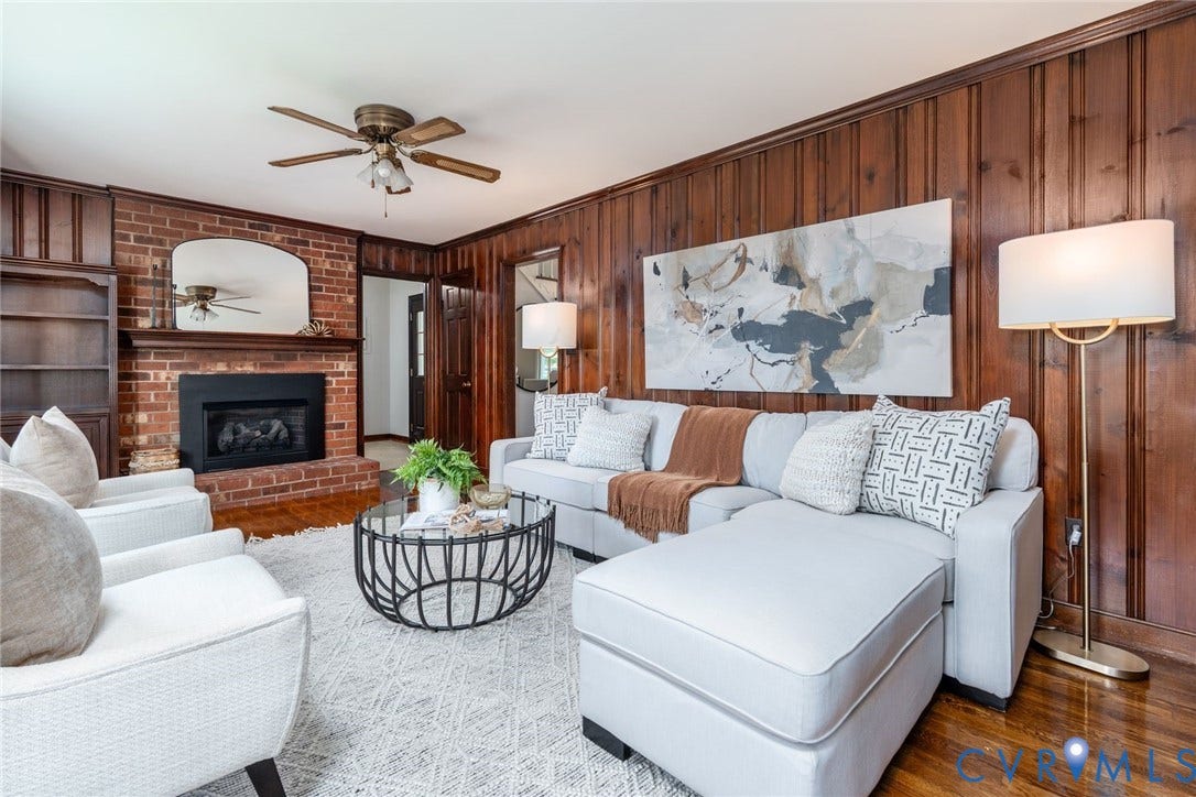 14613 Gimbel Drive, Chester, VA 23836 Brick fireplace with a dark mantel, wood-paneled walls, built-in shelving, wood-finish flooring, and a ceiling fan