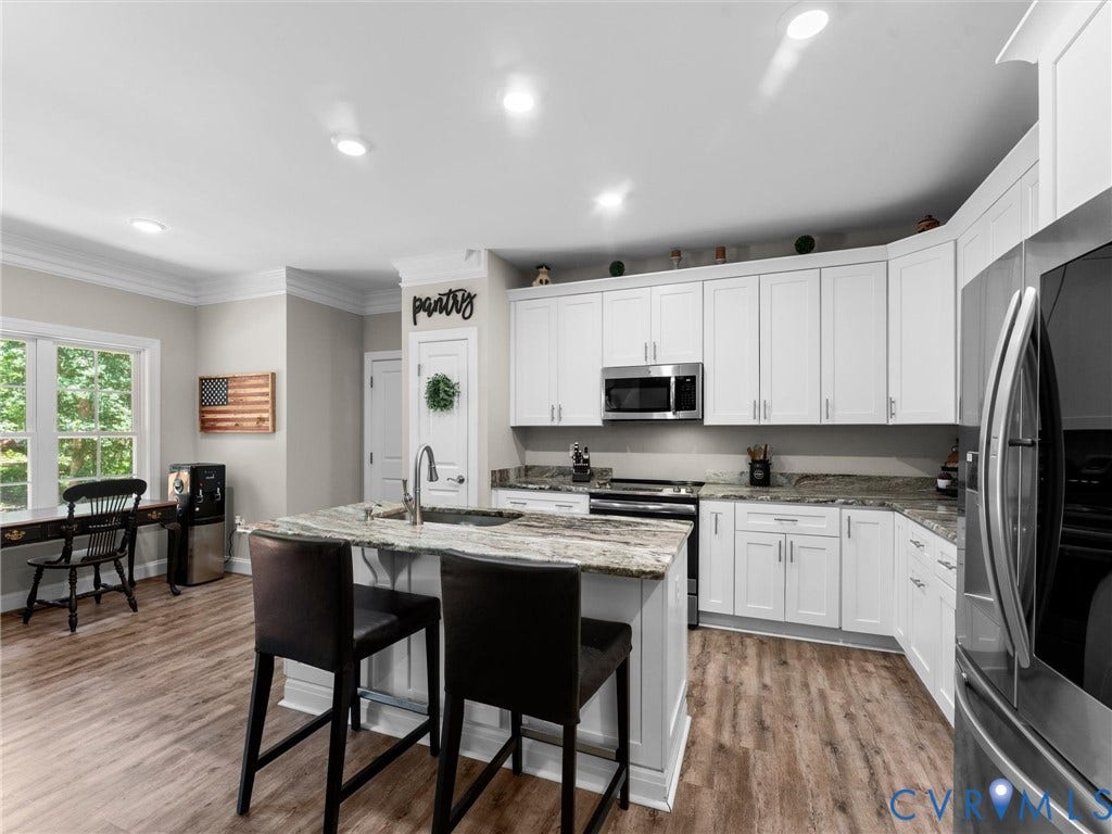 8200 Madeline Court, Strath Woods, Henrico, VA 23231 Open-concept kitchen featuring an island with seating, white shaker-style cabinetry, stainless steel appliances, and wood-finish flooring