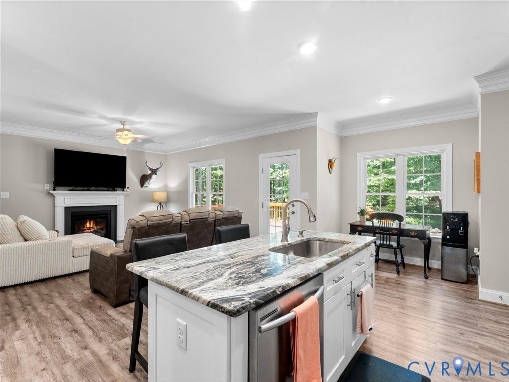 8200 Madeline Court, Strath Woods, Henrico, VA 23231 Open-concept living space featuring a kitchen island with stone-finish countertop and undermount sink, wood-finish flooring, a fireplace with a white mantel, and crown molding