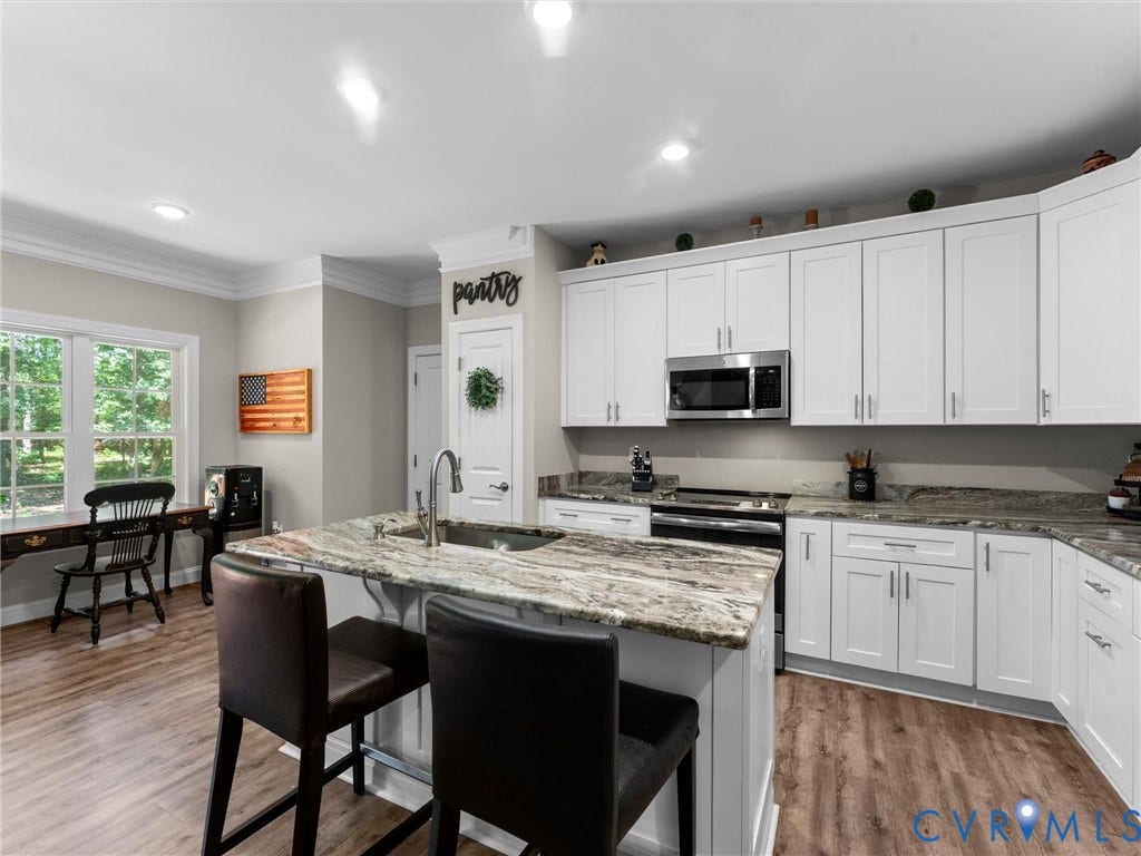 8200 Madeline Court, Strath Woods, Henrico, VA 23231 Spacious kitchen featuring an island with a built-in sink, white cabinetry, integrated stainless steel microwave, and wood-finish flooring