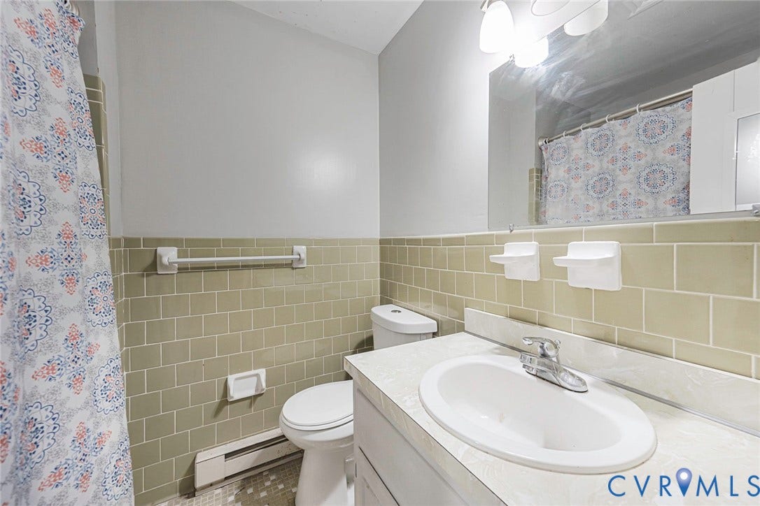 124 Northfield Lane, North Chesterfield, VA 23236 Bright bathroom featuring subway tile wainscoting in soft sage tones, dual vanity with white countertop and integrated sink, large framed mirror with integrated lighting, and ceramic tile flooring