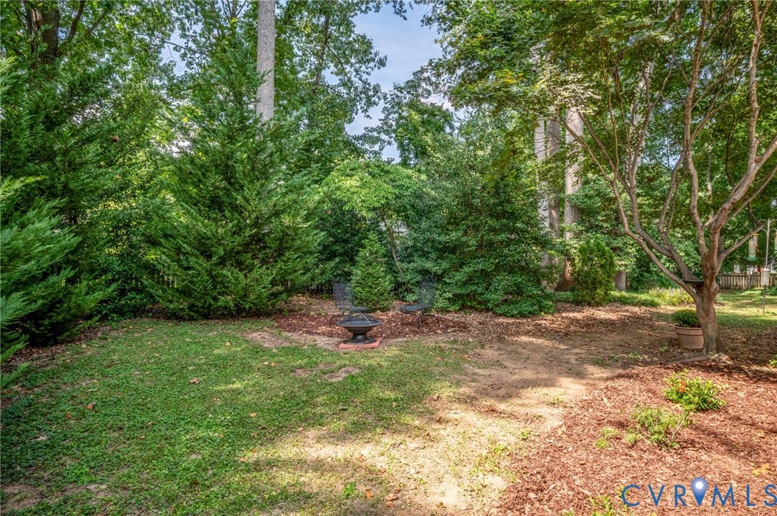 3704 Milbrier Place, Henrico, VA 23233 Manicured lawn, mature trees, fire pit with stone surround, natural mulch landscaping, and dense perimeter plantings