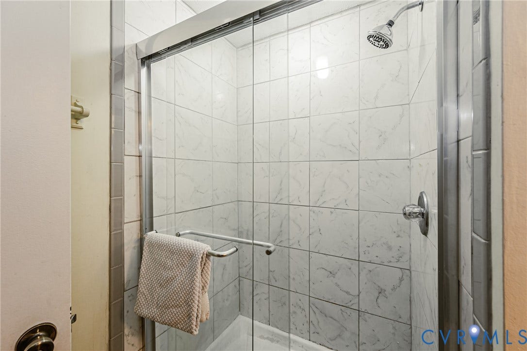 9406 Emmett Court, Glen Allen, VA 23060 Spa-inspired shower enclosure featuring marble-look tile walls, chrome framed glass sliding doors, rainfall showerhead, and dual wall-mounted fixtures