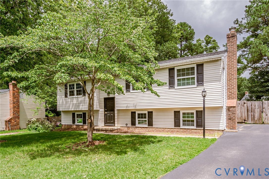 9406 Emmett Court, Glen Allen, VA 23060 Charming split-level home featuring brick and vinyl siding exterior, mature landscaping with established trees, paved driveway, multiple windows with dark shutters, and a manicured lawn