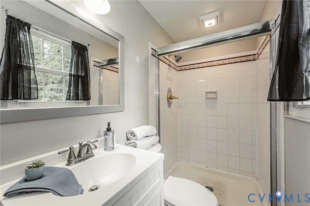 9406 Emmett Court, Glen Allen, VA 23060 Full bathroom featuring a white vanity with integrated sink, brushed nickel faucet, large framed mirror, and a shower with white subway tile and decorative border