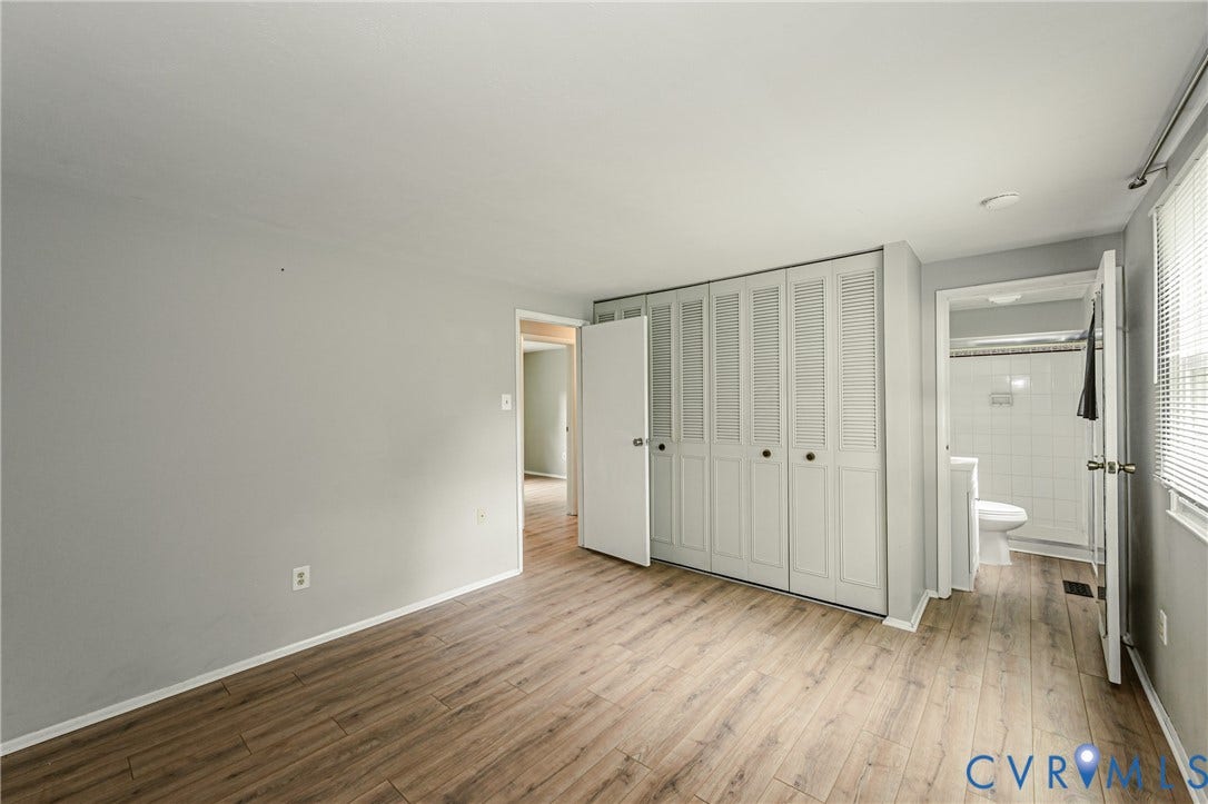9406 Emmett Court, Glen Allen, VA 23060 Spacious bedroom featuring warm wood-finish flooring, abundant natural light from multiple windows, and a trio of white bi-fold closet doors providing generous storage