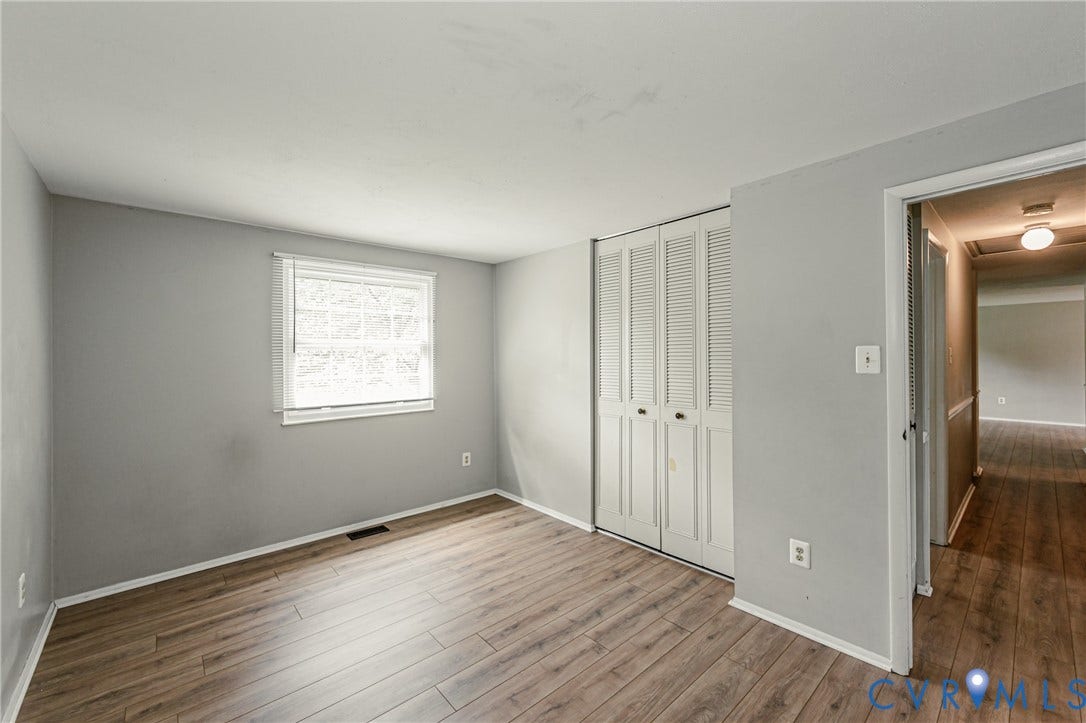 9406 Emmett Court, Glen Allen, VA 23060 Spacious bedroom featuring pristine wood-finish flooring, neutral gray walls, and abundant natural light from a large casement window