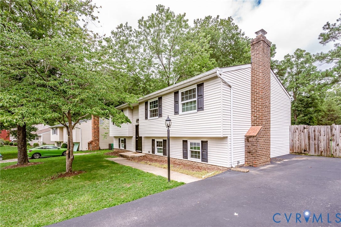 9406 Emmett Court, Glen Allen, VA 23060 Split-level home featuring white vinyl siding with a brick chimney, two-car driveway with asphalt surface, and a manicured front lawn with mature shade trees
