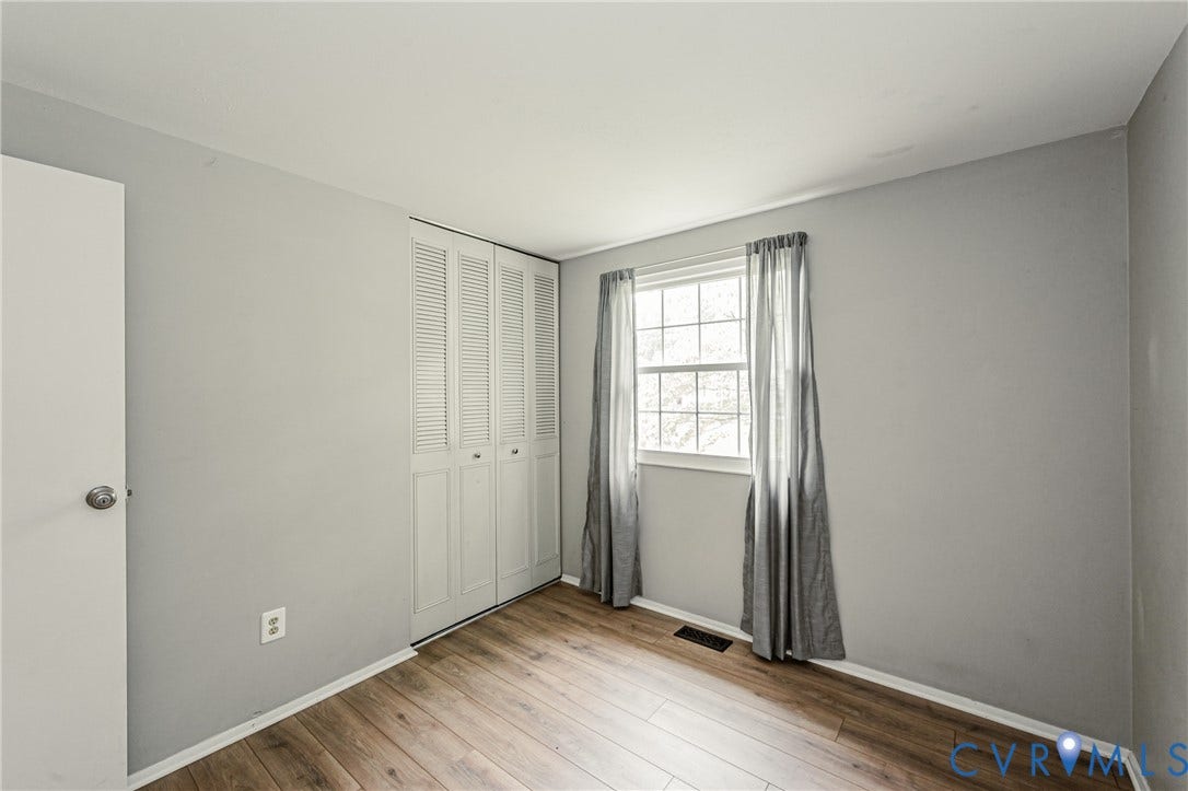 9406 Emmett Court, Glen Allen, VA 23060 Bright bedroom featuring hardwood flooring, generous natural light from large double-hung window with custom drapery, louvered closet doors, and neutral wall finishes throughout