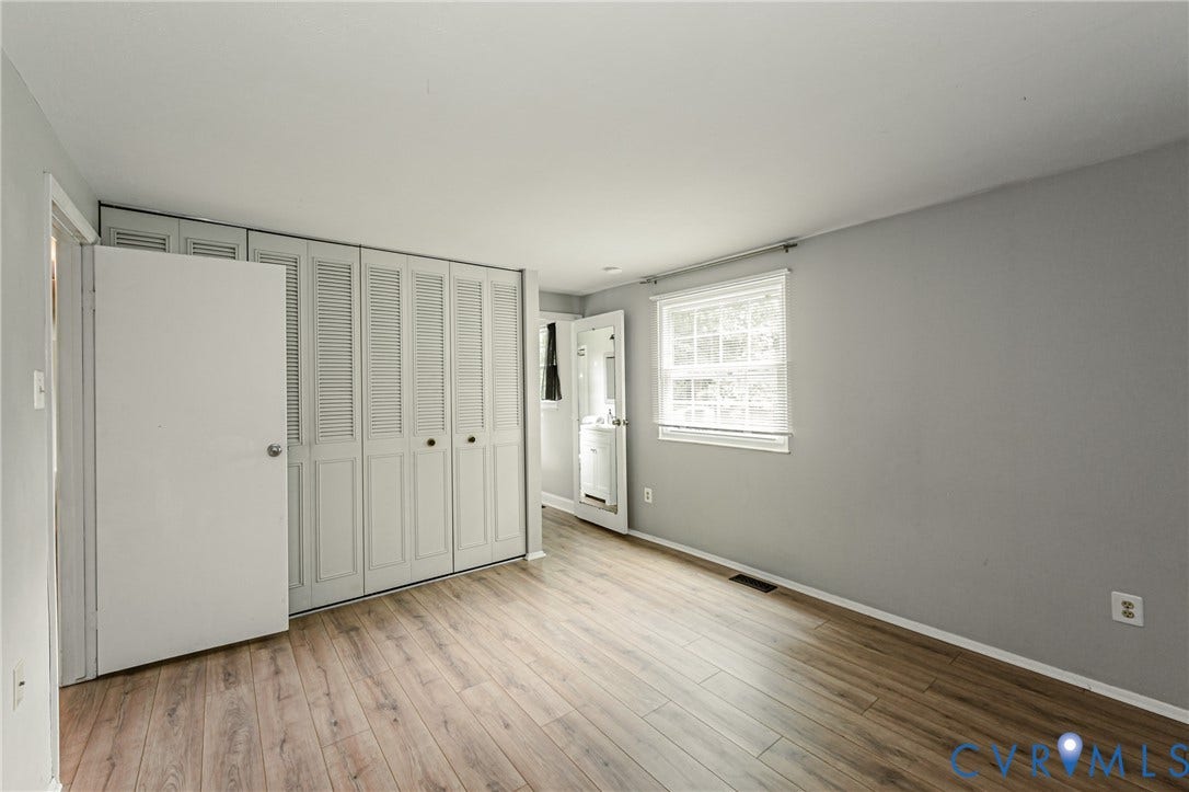 9406 Emmett Court, Glen Allen, VA 23060 Spacious bedroom showcasing wood-finish flooring, abundant natural light from a large window, and an expansive closet system with louvered bi-fold doors