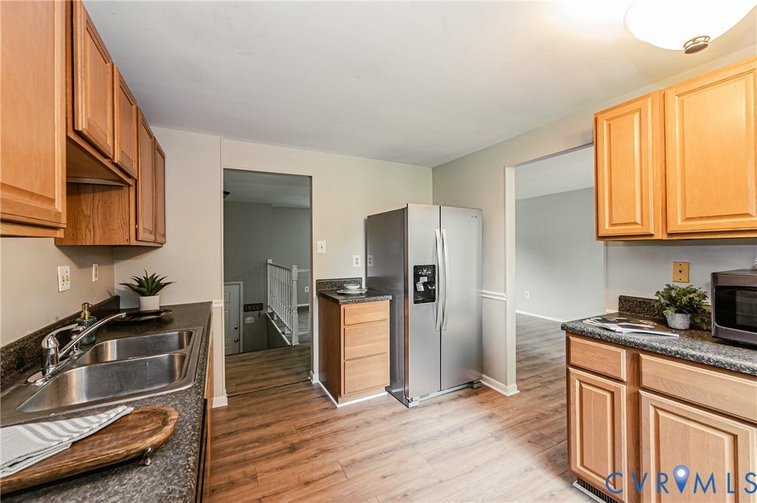 9406 Emmett Court, Glen Allen, VA 23060 Spacious kitchen featuring warm wood-finish cabinetry with raised-panel doors, stainless steel appliances including a side-by-side refrigerator, granite countertops, and wood-finish flooring throughout