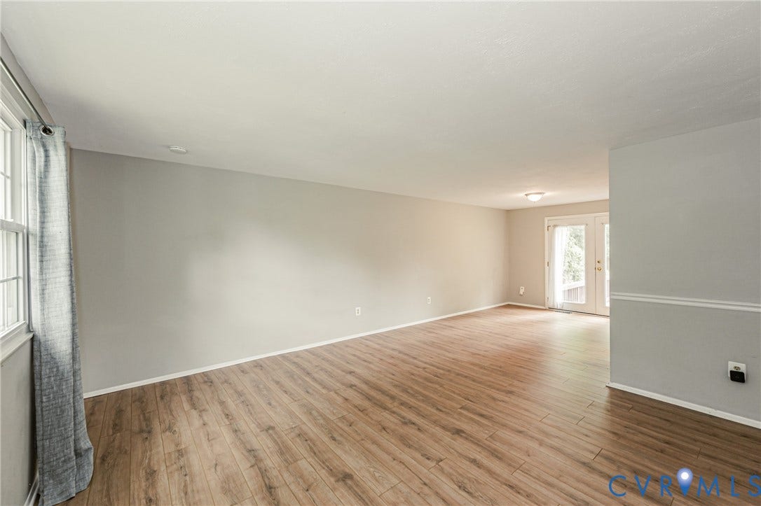 9406 Emmett Court, Glen Allen, VA 23060 Spacious open-concept living area featuring warm wood-finish flooring throughout, neutral wall finishes with wainscoting detail, recessed ceiling lighting, and abundant natural light from multiple windows