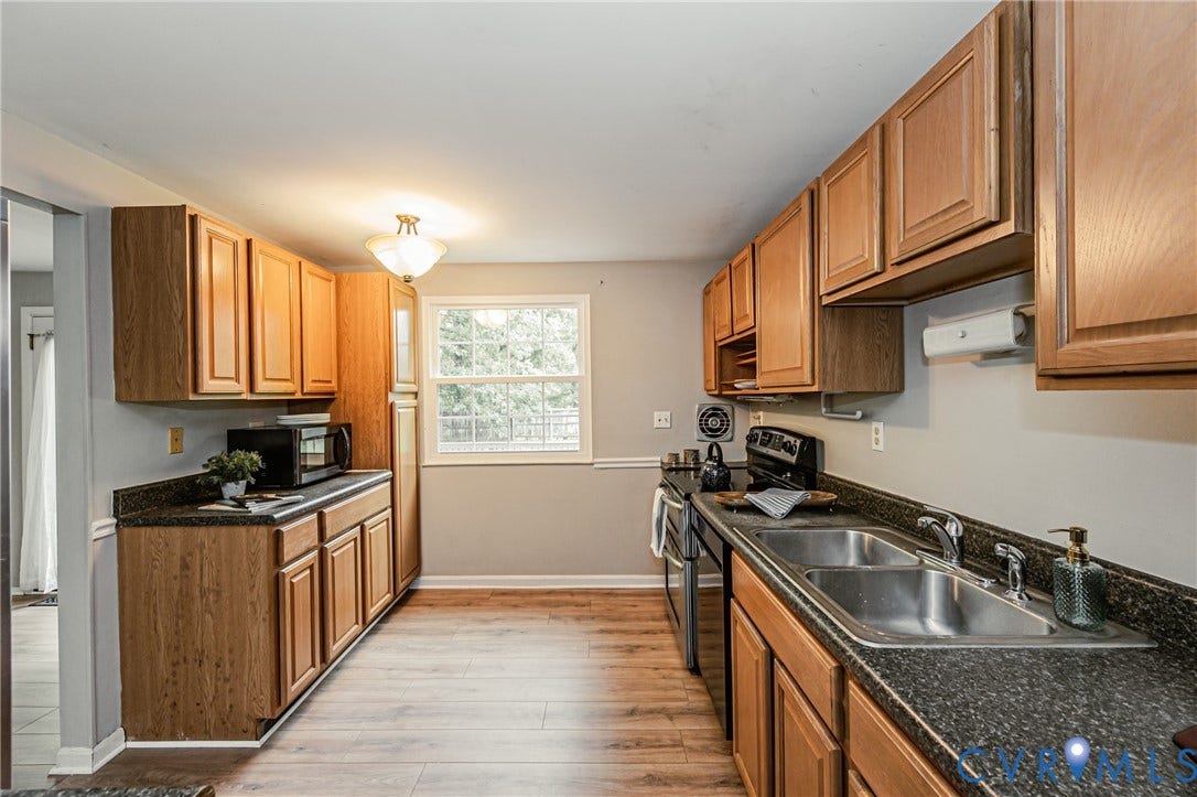 9406 Emmett Court, Glen Allen, VA 23060 Galley kitchen featuring wood-finish cabinetry, dual stainless steel sinks with granite countertops, black appliances, and wood-finish flooring throughout