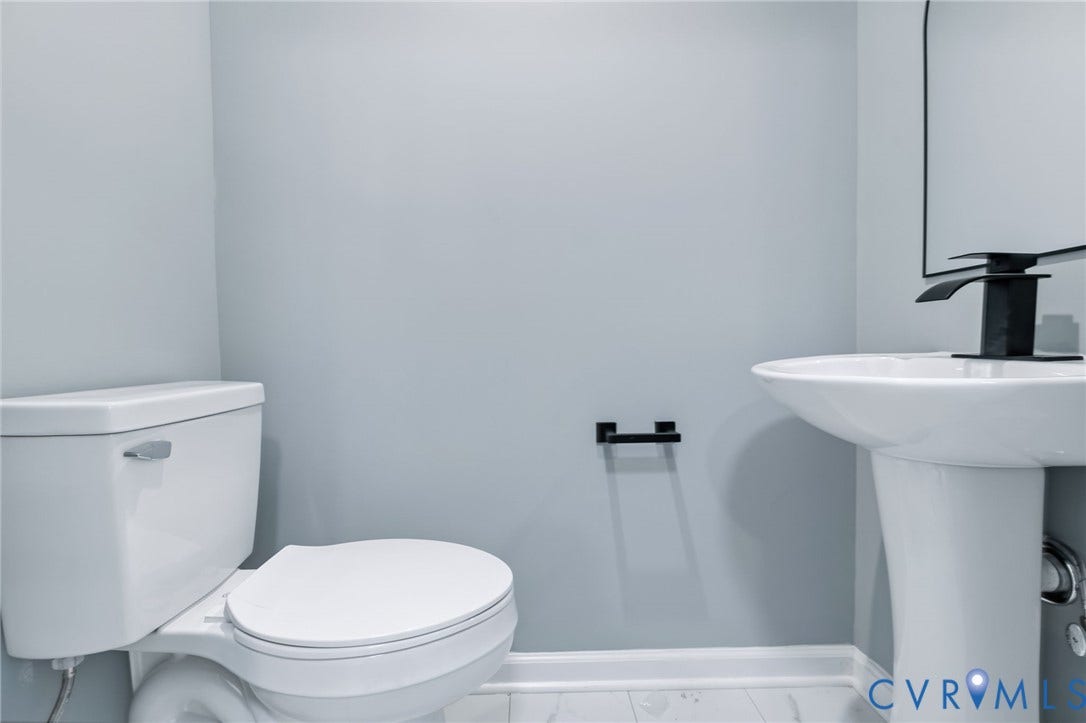 Pedestal sink with a matte black waterfall faucet, white toilet, and light-toned walls